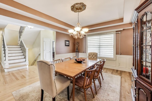 dining space with a chandelier, light wood-type flooring, a wainscoted wall, a decorative wall, and stairs