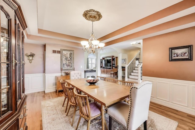 dining room featuring decorative columns, light wood-style floors, a decorative wall, arched walkways, and a wainscoted wall