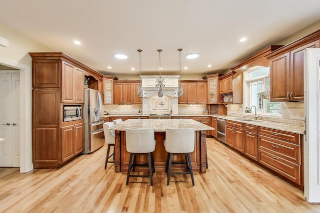 kitchen with stainless steel appliances, a sink, a center island, a breakfast bar, and light wood finished floors