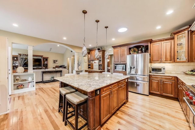 kitchen featuring appliances with stainless steel finishes, decorative columns, arched walkways, light wood-type flooring, and recessed lighting