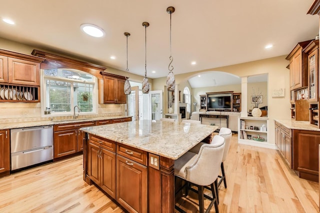 kitchen featuring stainless steel dishwasher, a sink, arched walkways, ornate columns, and a breakfast bar