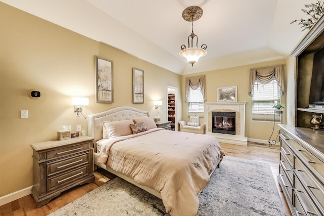 bedroom featuring baseboards, a glass covered fireplace, and light wood-style floors