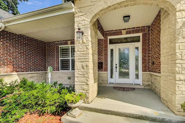 entrance to property with stone siding, a porch, and brick siding