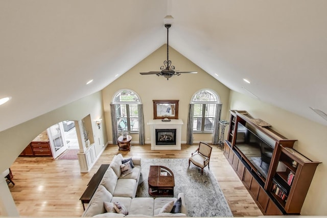 living area with a glass covered fireplace, ceiling fan, healthy amount of natural light, light wood-type flooring, and lofted ceiling