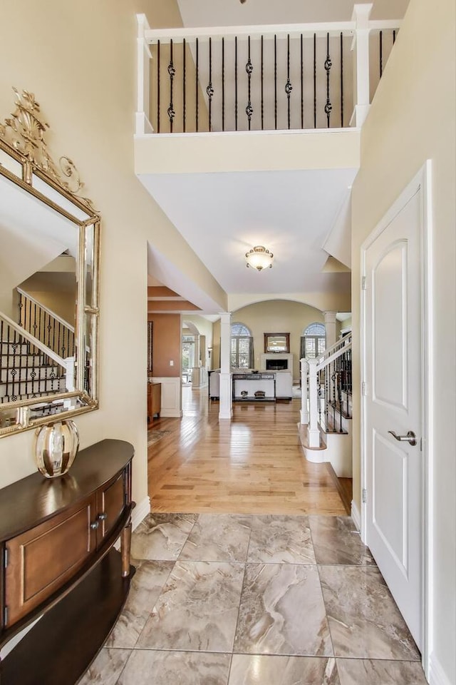 entrance foyer with ornate columns, stairway, marble look tiles, and a high ceiling