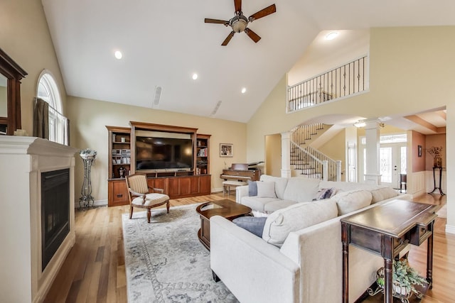 living area with ornate columns, high vaulted ceiling, ceiling fan, a fireplace, and wood finished floors