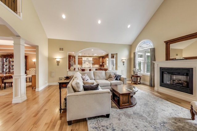 living room with high vaulted ceiling, decorative columns, light wood-type flooring, arched walkways, and recessed lighting