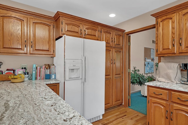 1002 Birchwood Ct, Morris, IL 60450 - kitchen featuring white refrigerator with ice dispenser, brown cabinets, light wood finished floors, backsplash, and light stone counters
