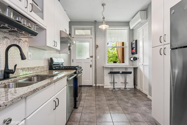 kitchen with stainless steel appliances, under cabinet range hood, a sink, decorative backsplash, and white cabinets