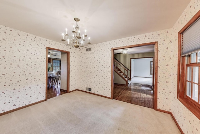 empty room with wallpapered walls, a chandelier, carpet floors, stairway, and a ceiling fan