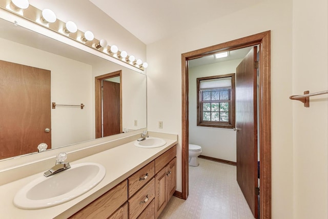 bathroom featuring toilet, double vanity, baseboards, and tile patterned floors