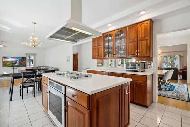 kitchen with island range hood, white appliances, light tile patterned floors, light countertops, and a chandelier