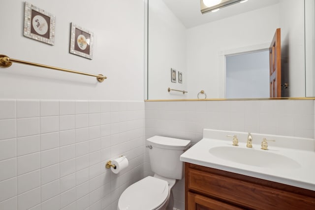 half bath featuring toilet, vanity, tile walls, and wainscoting