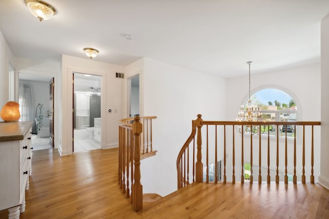 corridor with an upstairs landing, light wood-style floors, a chandelier, and baseboards