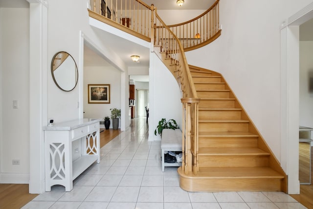entryway with a towering ceiling, stairway, light tile patterned floors, and baseboards