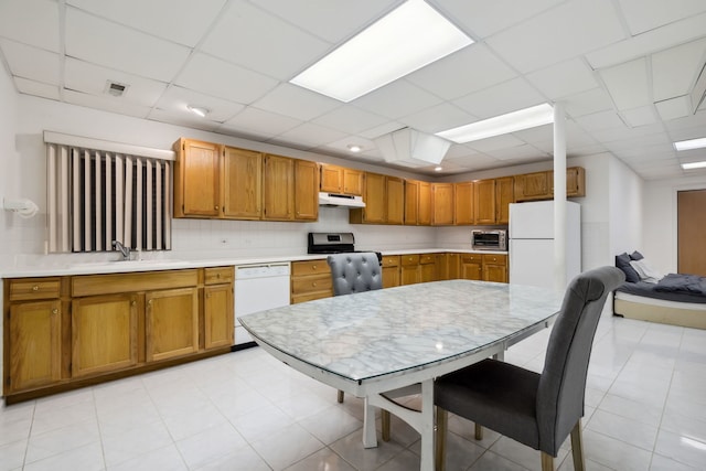 kitchen with white appliances, a sink, under cabinet range hood, light countertops, and brown cabinets