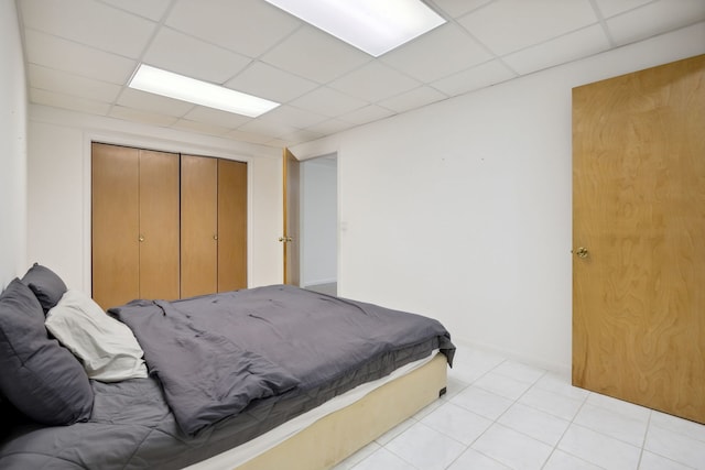 bedroom with a paneled ceiling, a closet, and light tile patterned floors