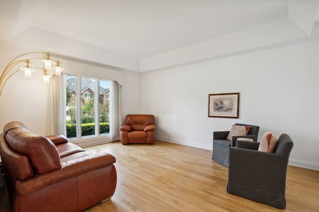 sitting room with light wood-type flooring, a tray ceiling, baseboards, and a chandelier