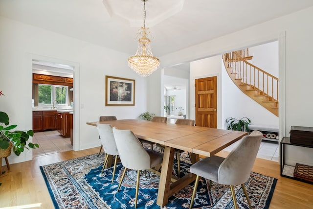 dining space with a chandelier, stairs, light wood finished floors, and ceiling fan