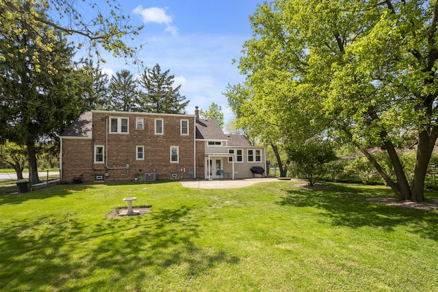 rear view of house with a patio area, a lawn, a chimney, and brick siding