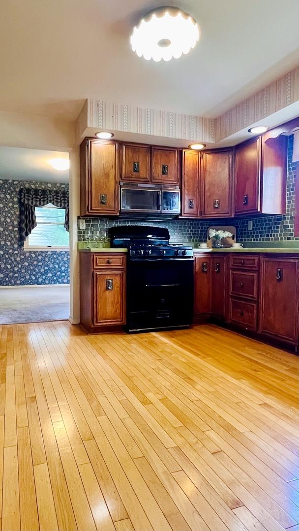 1305 Baugh Dr, Normal, IL 61761 - kitchen featuring black range with gas cooktop, stainless steel microwave, light wood-style flooring, wallpapered walls, and backsplash