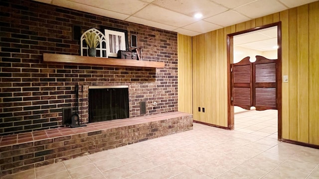 1305 Baugh Dr, Normal, IL 61761 - unfurnished living room with light tile patterned flooring, wooden walls, a brick fireplace, baseboards, and a paneled ceiling