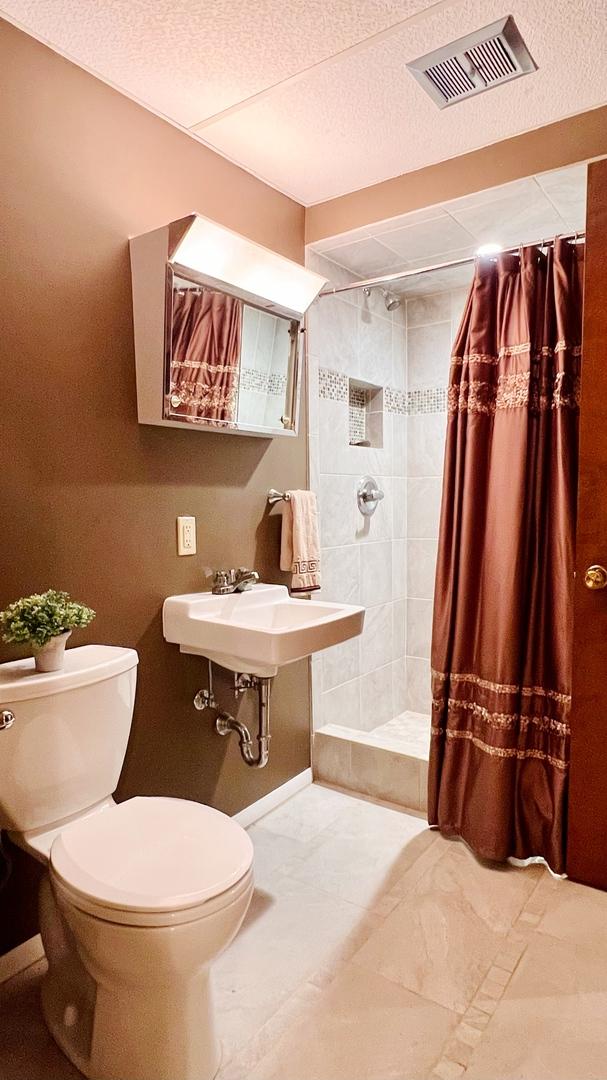 1305 Baugh Dr, Normal, IL 61761 - bathroom with toilet, a shower stall, a textured ceiling, a sink, and baseboards