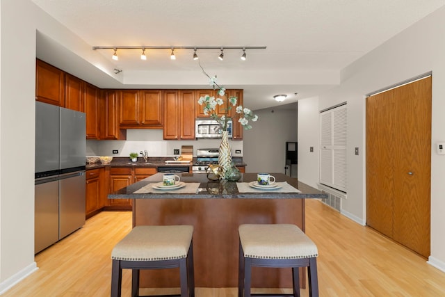kitchen with stainless steel appliances, light wood-style floors, dark countertops, and a breakfast bar