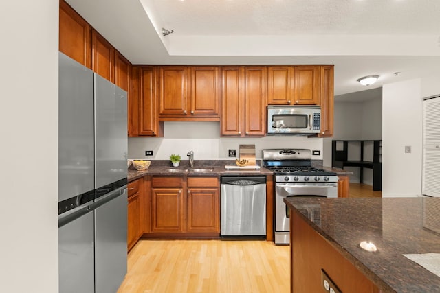 kitchen with appliances with stainless steel finishes, a sink, light wood-style floors, and brown cabinetry