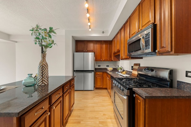 kitchen featuring appliances with stainless steel finishes, light wood finished floors, brown cabinetry, and a textured ceiling