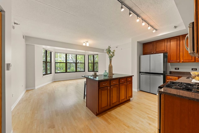 kitchen with appliances with stainless steel finishes, a textured ceiling, open floor plan, track lighting, and light wood-type flooring