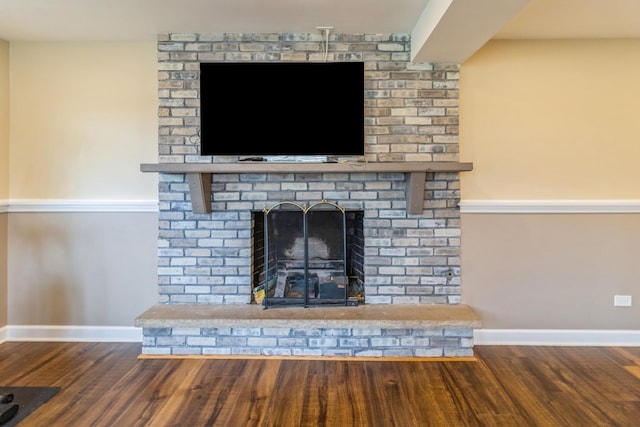 detailed view of wood finished floors, a brick fireplace, and baseboards