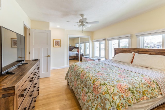 bedroom with light wood finished floors, a closet, multiple windows, and ceiling fan