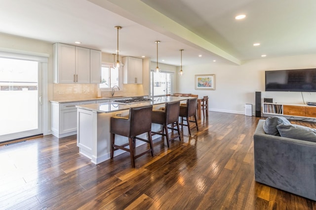 kitchen featuring open floor plan, dark wood-style flooring, a kitchen breakfast bar, a sink, and an island with sink