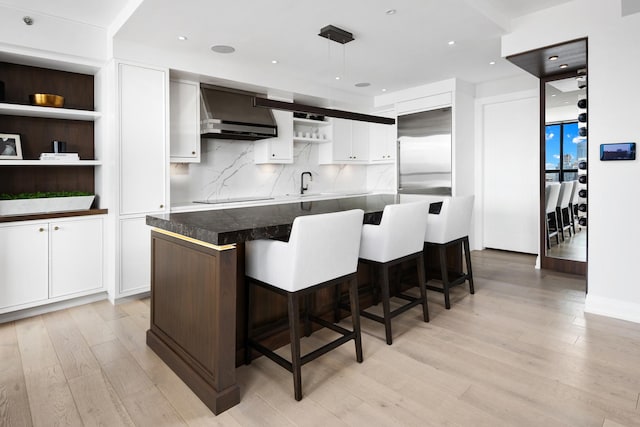 kitchen featuring open shelves, wall chimney exhaust hood, built in fridge, light wood-type flooring, and white cabinetry