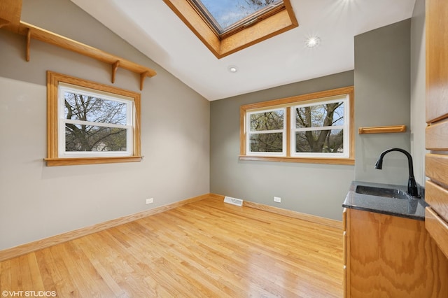 spare room featuring a sink, a skylight, healthy amount of natural light, wood finished floors, and lofted ceiling