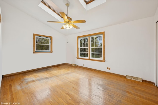 empty room featuring a skylight, lofted ceiling, light wood-type flooring, a ceiling fan, and baseboards