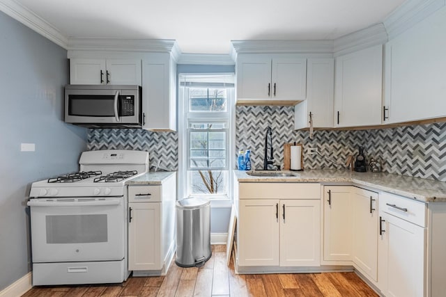 kitchen featuring stainless steel microwave, white gas range, a sink, ornamental molding, and light wood-type flooring