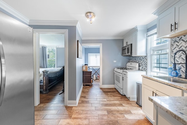 kitchen featuring stainless steel appliances, a sink, backsplash, light wood-style flooring, and light stone counters