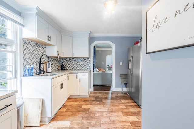 kitchen featuring stainless steel fridge, a sink, arched walkways, tasteful backsplash, and white cabinets