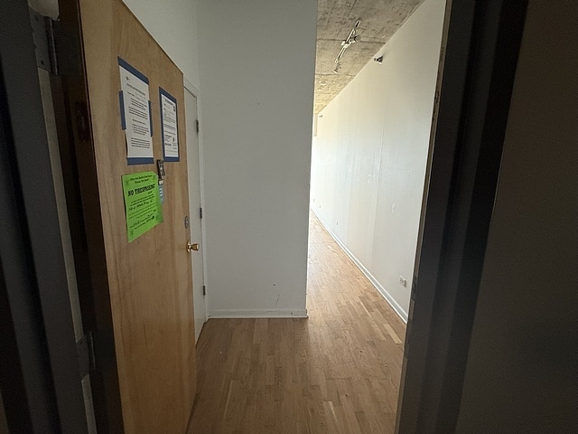 hallway featuring light wood-style flooring, rail lighting, and baseboards