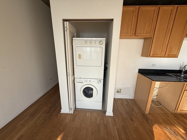 clothes washing area featuring stacked washer / drying machine, dark wood-style floors, and baseboards