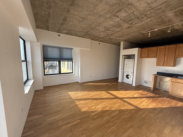 unfurnished living room with estacked washer and dryer, baseboards, and wood finished floors