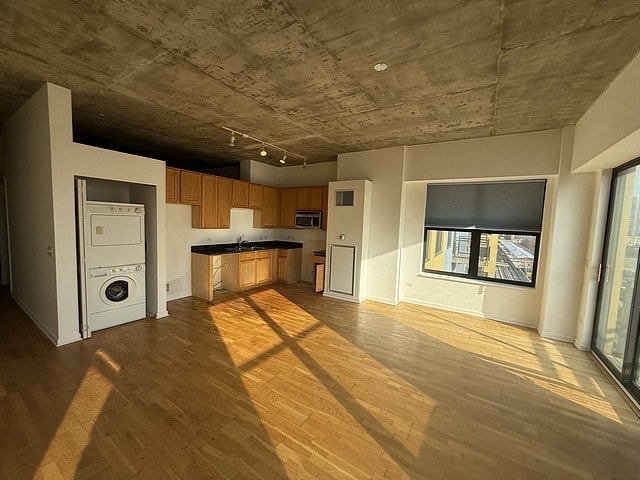 kitchen with stacked washer / drying machine, a sink, stainless steel microwave, wood finished floors, and dark countertops