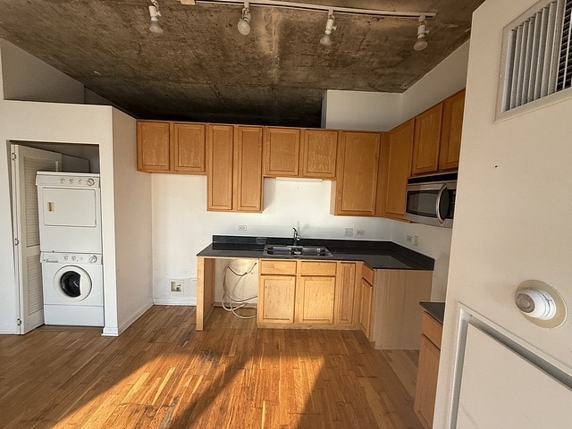 kitchen with rail lighting, estacked washer and dryer, stainless steel microwave, a sink, and wood finished floors