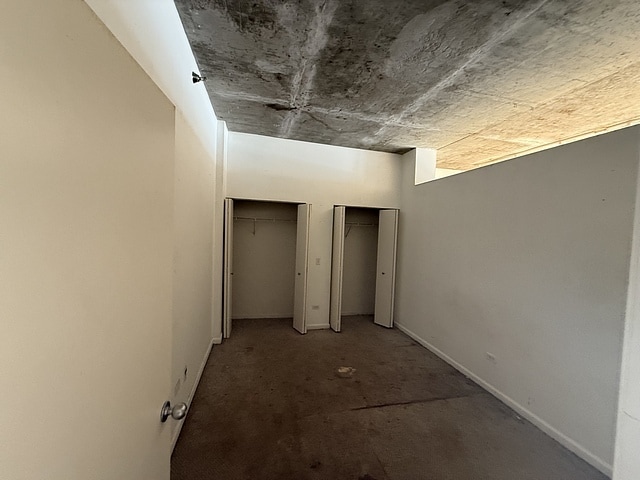 unfurnished bedroom with two closets, baseboards, and concrete floors