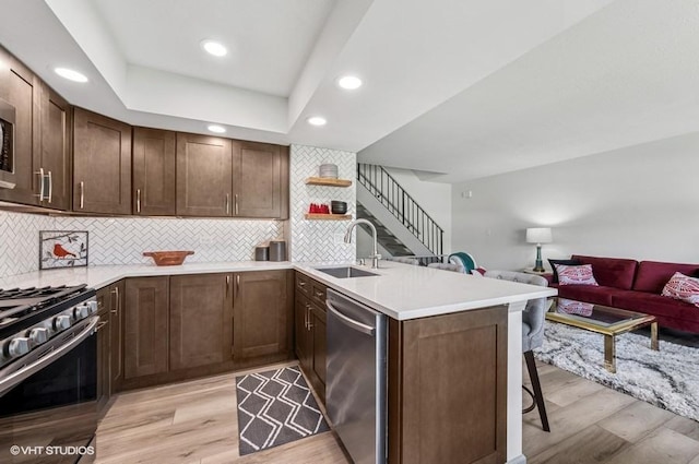 kitchen featuring a sink, appliances with stainless steel finishes, a peninsula, a breakfast bar, and open floor plan