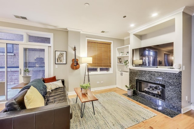 living area featuring wood finished floors, ornamental molding, a high end fireplace, baseboards, and built in shelves