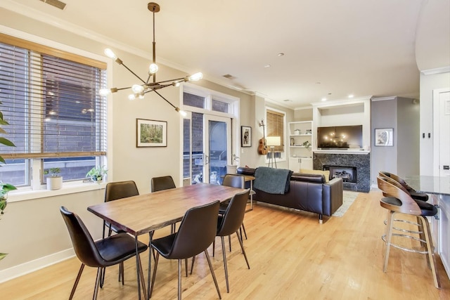 dining space with a fireplace, crown molding, a chandelier, light wood finished floors, and baseboards