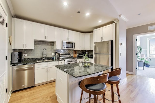 kitchen featuring stainless steel appliances, a sink, light wood-type flooring, decorative backsplash, and dark stone counters